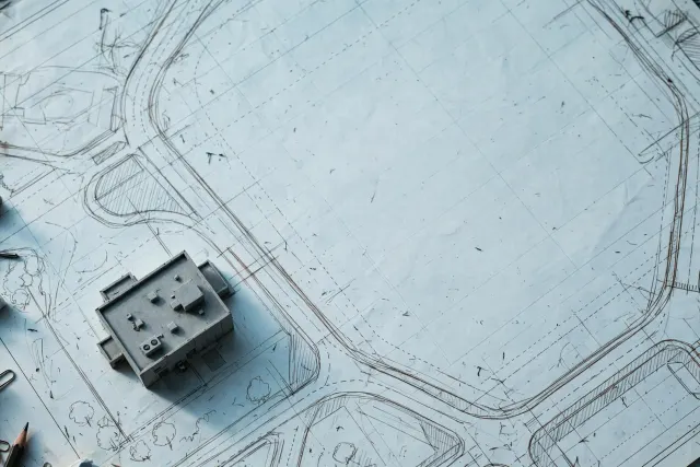 Illustrasjon: en liten ferdig modell av et datasenter står på et stort arkitekttegningsark der resten av tomten kun er tomme blyantkonturer og stiplete byggeplaner, sett ovenfra i kjølig dagslys.