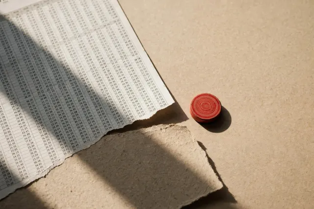 Illustrasjon: En trykt benchmark-rapport med tallsøyler der nedre halvdel er revet av og viser blankt papir, med en ubrukt rød kontrollstempel liggende ved siden av, fotografert ovenfra i hardt dagslys.