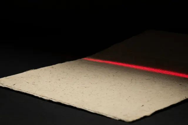 Illustrasjon: et kremfarget papirark der et svakt, skjult mønster av tråder bare blir synlig der skrått lys treffer overflaten – en metafor for usynlige tekstvannmerker.