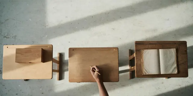 Illustrasjon: tre skolepulter sett ovenfra med ulikt innhold, som symboliserer aldersdelerte regler for generativ AI i norske skoler.