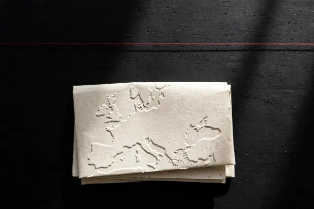 Illustrasjon: Et foldet papirkart over Europa på et mørkt bord, med en stram rød tråd hengende like over kartet, utenfor rekkevidde.