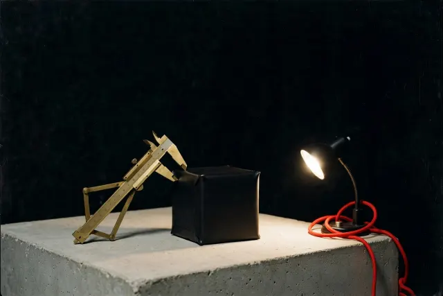 Illustrasjon: en forseglet, ugjennomsiktig kube undersøkes med måleverktøy og en enkelt inspektør­lampe, uten at innholdet kan ses.