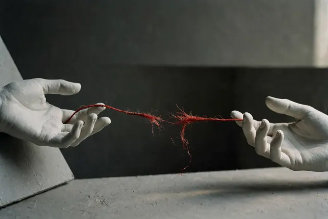 Illustration: Two pale ceramic hands on either side of a dark void, connected by a thin red thread snapped in the middle, evoking chatbots that recognize mental distress but fail to connect users to help.
