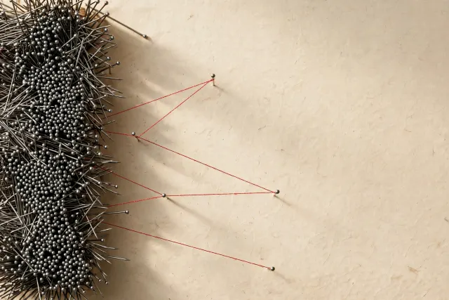 Illustration: hundreds of steel pins on a wall with a few red threads connecting scattered pins into clear paths, a metaphor for the 547 search tasks in the ATLAS benchmark.