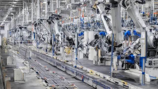 Robotarmer arbeider langs et samlebånd i en lys fabrikkhall.