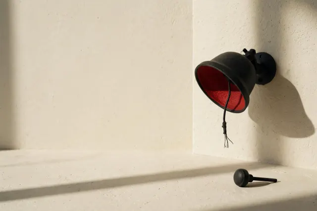Illustration: A black alarm bell on a cream wall with its clapper removed and lying on the floor below, a loose severed wire hanging — a metaphor for alerts that never fire.