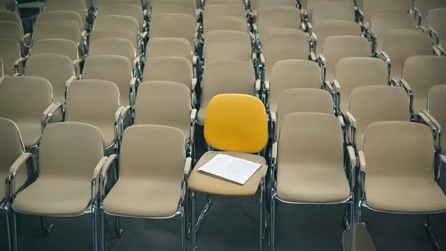 Illustrasjon: lange rekker av identiske tomme kontorstoler i en stor hall, der én eneste stol er trukket ut og i bruk – et bilde på lav adopsjon av Copilot-lisenser blant Office 365-brukerne.