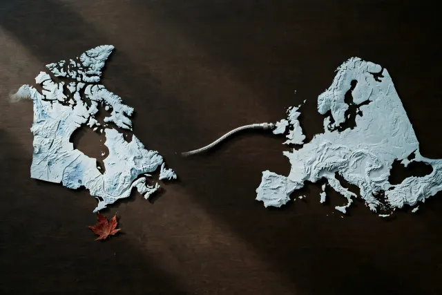 Illustration: Two paper relief maps, one of Canada and one of Europe, joined by a thick data cable across a dark table, in a restrained palette with a red maple-leaf accent.