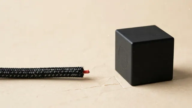 Illustrasjon: En tykk datakabel er klippet over og ligger adskilt fra en matt svart kube på lys bakgrunn, som symbol på at OpenAI har fjernet netttilgangen fra modellen Astra etter høyeste risikovurdering.
