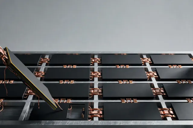 Illustration: A grid of identical matte black chips mounted in an aluminum frame with one chip lifted out — a metaphor for millions of mass-produced AI accelerators.