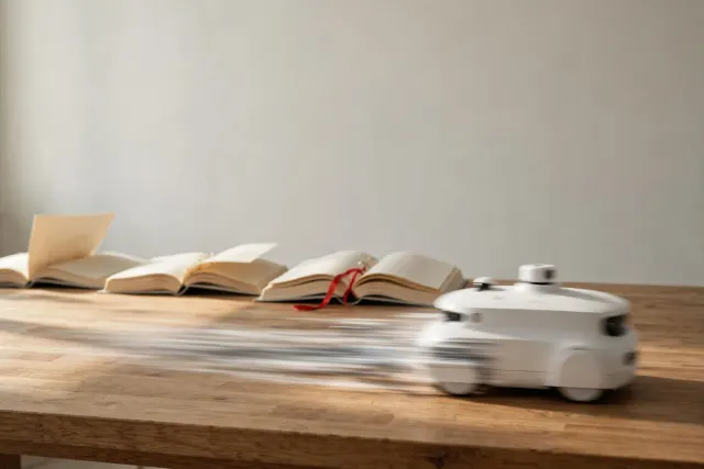 Illustrasjon: En hvit autonom enhet i bevegelse forlater tre tykke, tomme permakter langt bak seg på et bord, som et bilde på KI-agenter i fart mens regelverket henger etter.