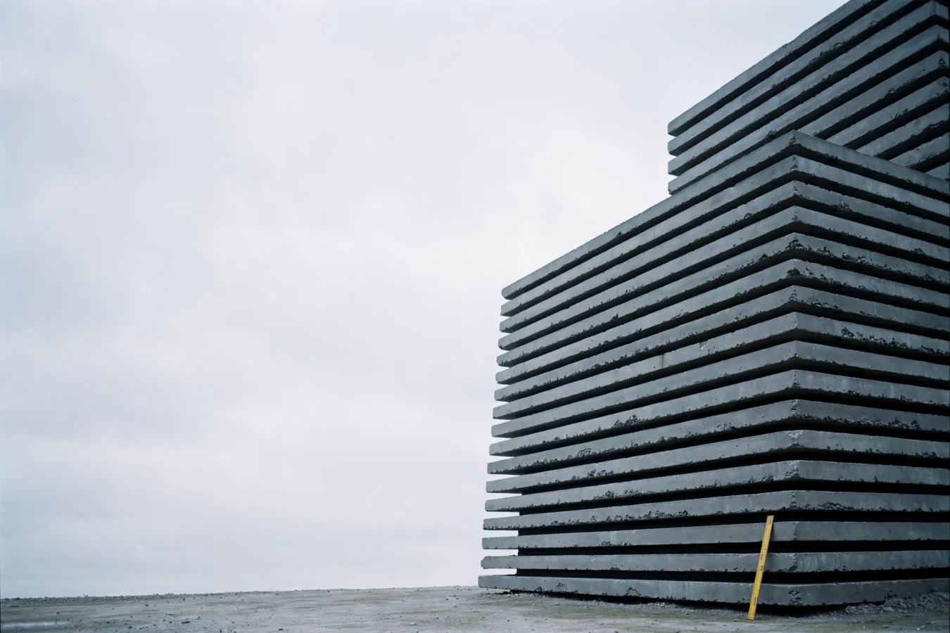 Illustration: A colossal concrete monolith fills the frame while a small yellow ruler at its base can measure only a fraction of the whole, reflecting a story about a giant language model whose efficiency figures are measured only by its own maker.