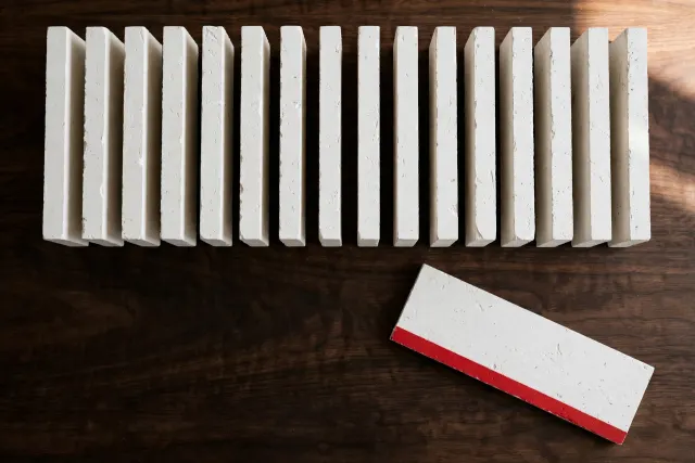 Twelve white regulatory blocks in a row on a table, one pulled forward and marked with a red stripe, illustrating the FSB's final AI practices where only one changed after objections.