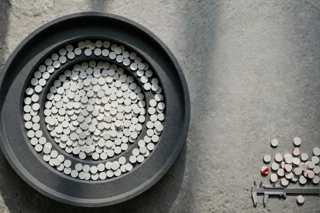 Illustration: hundreds of identical white voting tokens in a gray bowl-shaped tiered tray, with a small group tipped over and marked in red, beside a slim measuring gauge.
