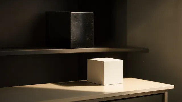 A heavy black cube sits shelved in shadow while a smaller plain white cube on a table below is lit by a sharp shaft of sunlight. Illustration.