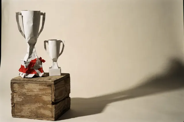 Two white paper trophies on a wooden pedestal, the taller one visibly snapped and taped back together — an illustration of an unverified top ranking.