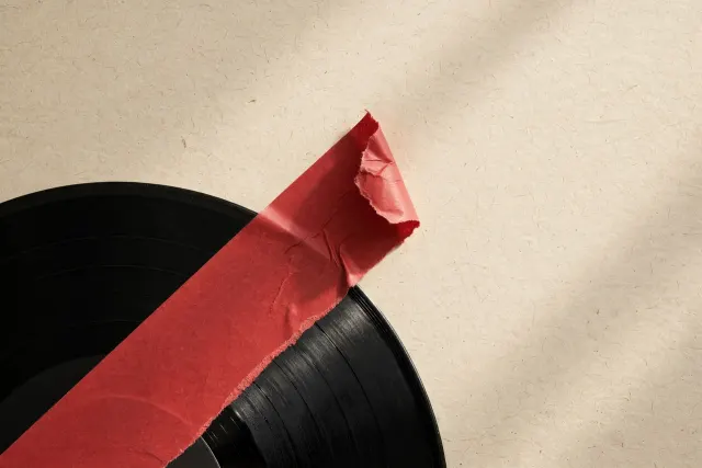 A vinyl record partially covered by a torn red label strip curling at the edge, seen from above.
