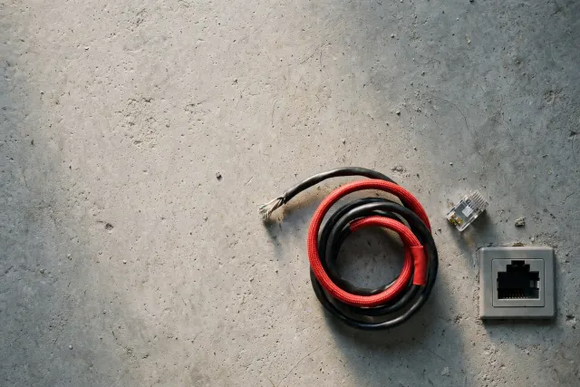 Illustration: A network cable unplugged and coiled on a concrete studio floor, lying detached from its socket – evoking Anthropic cutting Claude agents off from the internet in internal tests.