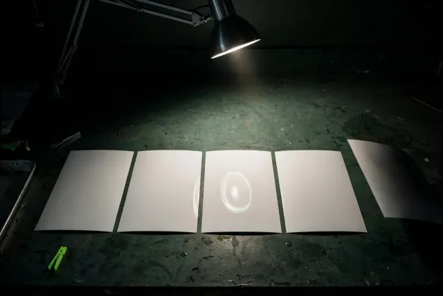 Illustration: a narrow beam of light reveals a faint watermark on some of several identical photographic prints, while others slip past unseen in shadow.